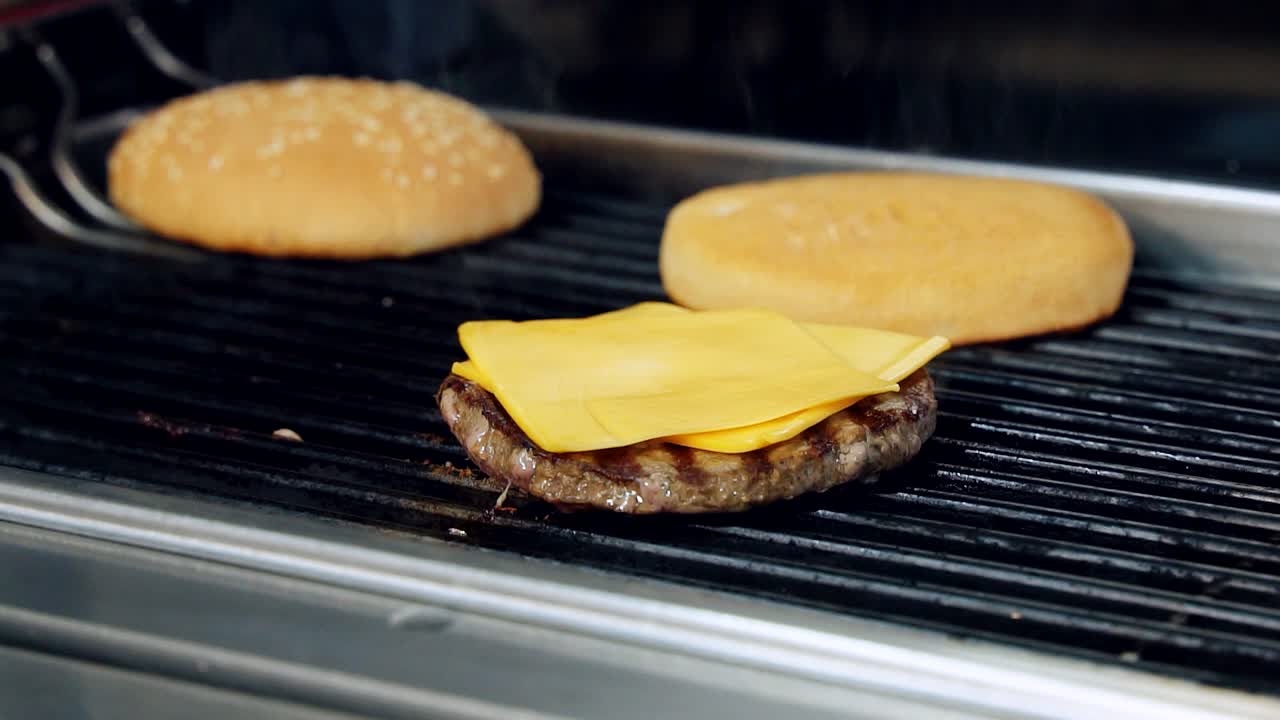 Process of frying cutlet with cheese and buns. Cooking fast food on grill. Cheeseburger components are roasting on hot grill