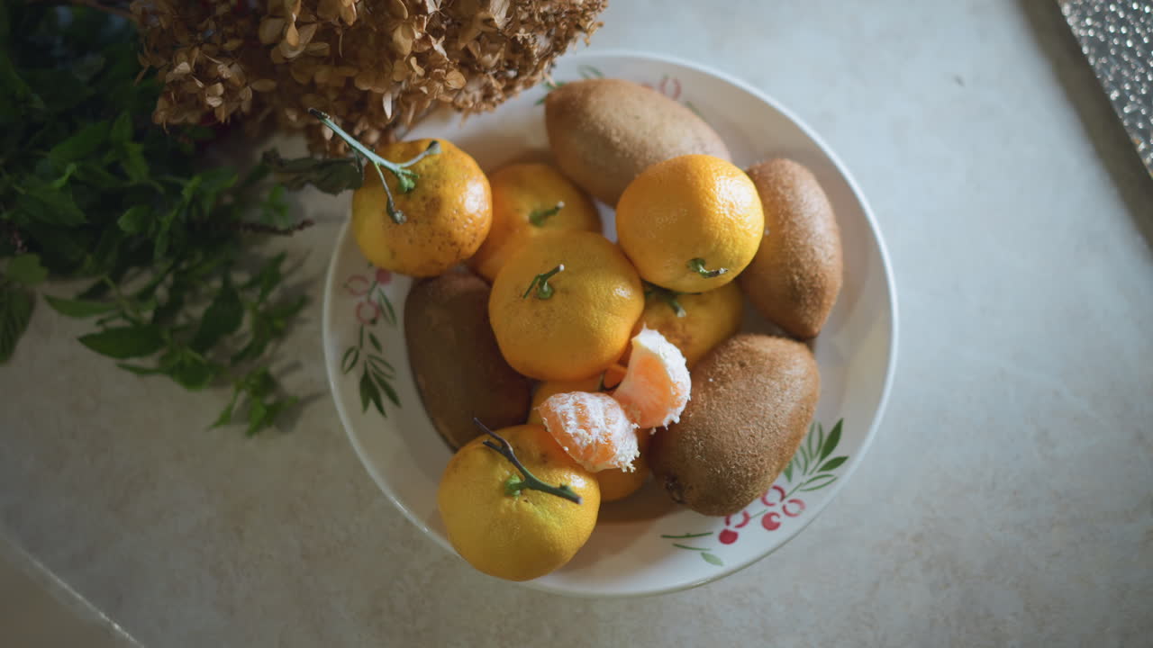 Tigela de Frutas na Bancada, Mexericas e Kiwis ao Lado de Hortênsia Seca sob Luz Natural Suave, Foto de Preparação Aconchegante de Cozinheiro Caseiro com Composição de Cima para Baixo Destacando Textura e Cor