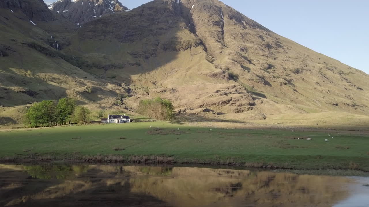 volando sobre el lago achtriochtan hacia una casa de campo en las tierras altas en un día soleado, glencoe, tierras altas escocesas, escocia