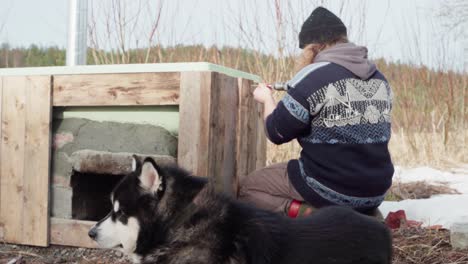 un hombre con su perro a su lado está usando un taladro para perforar agujeros en la tabla de madera para el revestimiento de la bañera de agua caliente - cerca