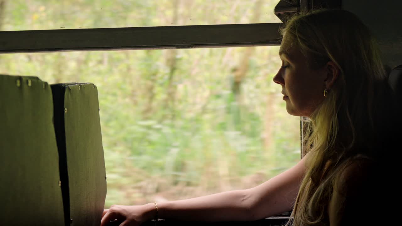A female traveler sits by the window of a scenic train in Sri Lanka, watching the lush tropical jungle go by along the Ella–Kandy route.
