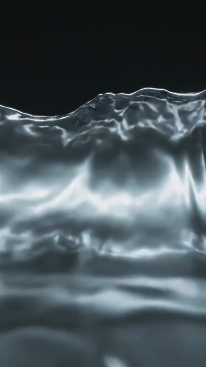 Video verticale: Impulso che spinge un liquido lucido che forma increspature e striature, ripreso da una prospettiva bassa su sfondo nero.