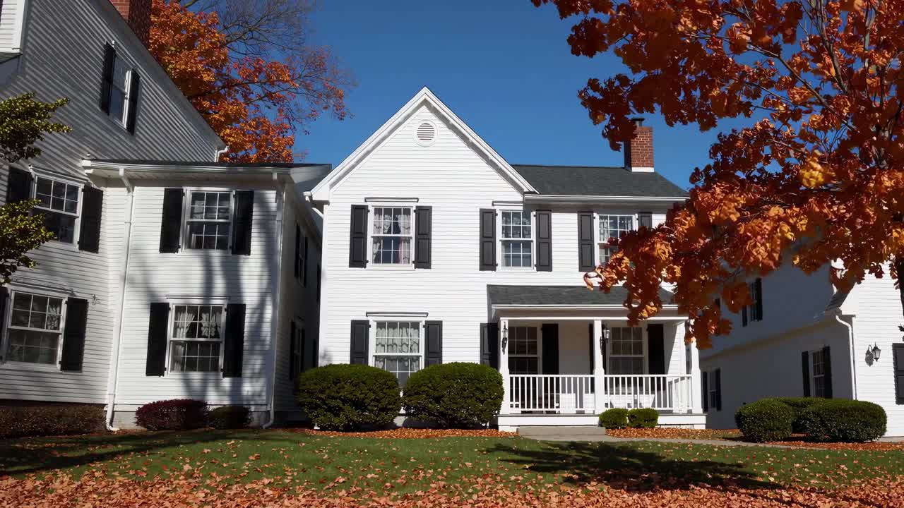 Charming white American house featuring classic black shutters and a welcoming porch, surrounded by a vibrant garden filled with colorful autumn foliage on a sunny day