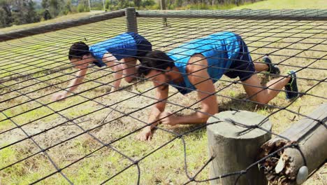 Fit-man-and-woman-crawling-under-the-net-during-obstacle-course