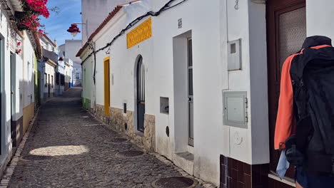 trekking woman with backpack walks narrow cobblestone lane in village