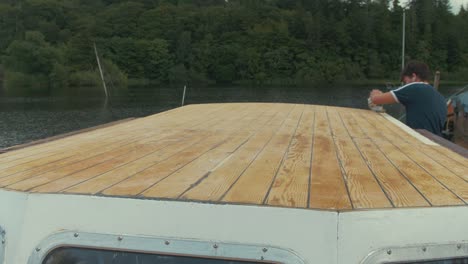 young man wipes down freshly sanded wooden boat roof