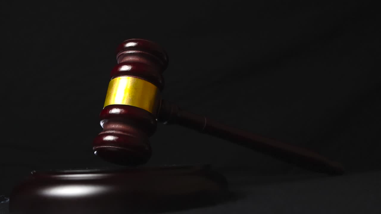 Close up video slowly moving around a wooden brown and decorated justice court gaol or hammer that is standing on its wooden pad in front of a black studio background
