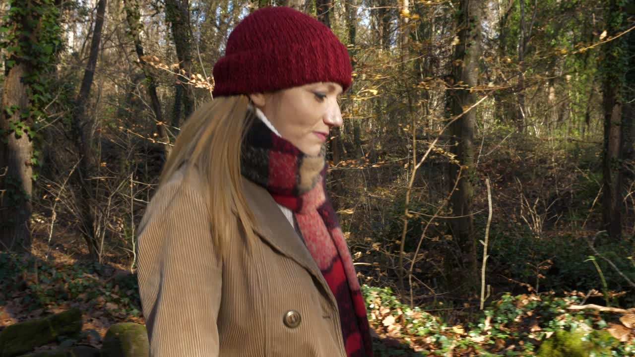 Kamerakjøring av en ung blond kvinne som går alene i en bøkeskog.