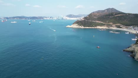drone aerial view in south korea countryside flying over the dark blue sea of busan next to a green mountain, ships and city in the background sunny day