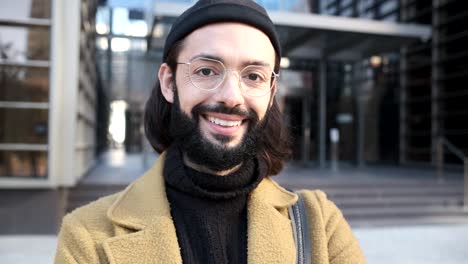 young man looking at the camera with a smile on his face while standing against an office building.