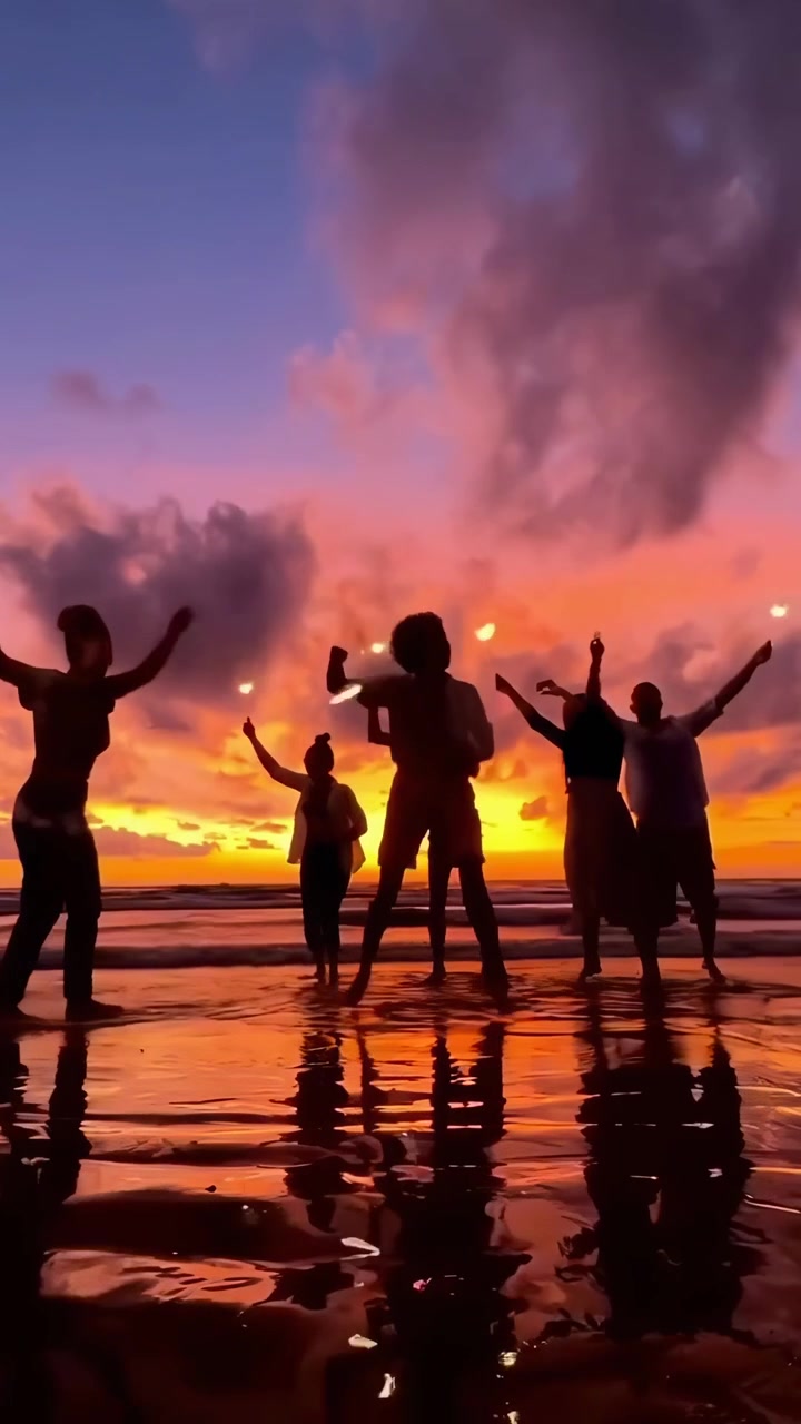 Gruppo di amici che ballano con stelle filanti sulla spiaggia al tramonto