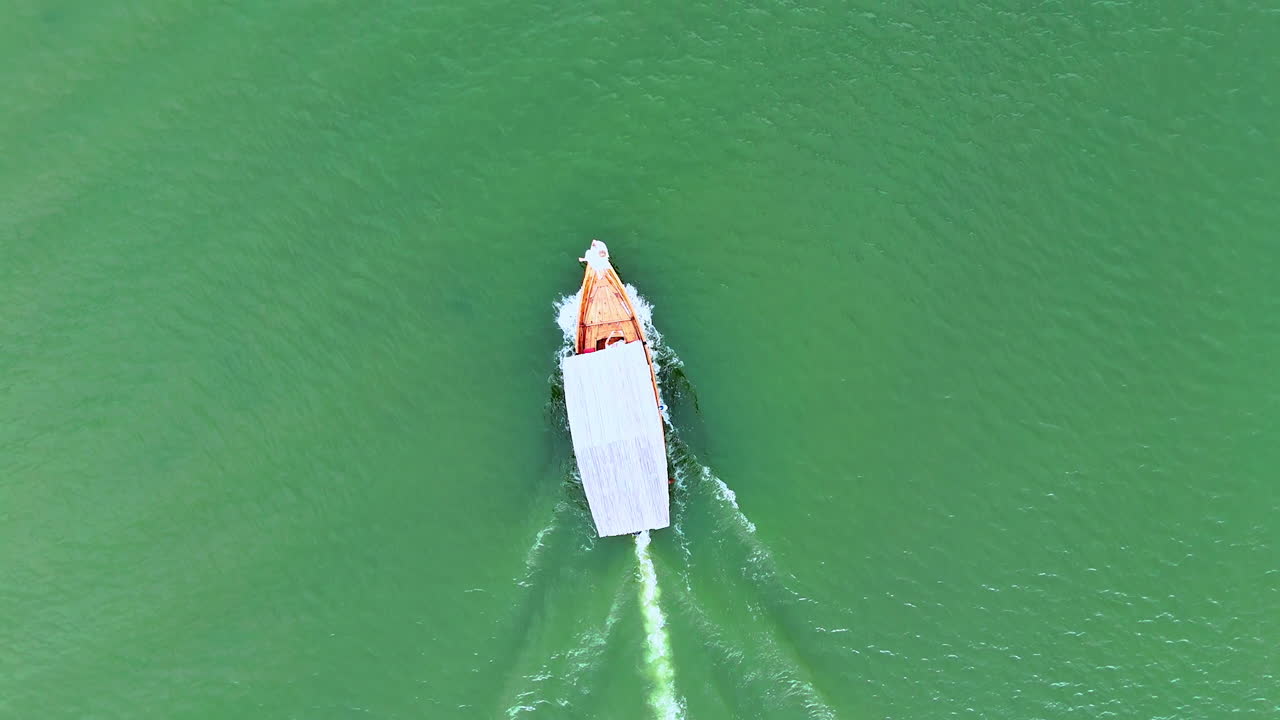 Boat covered with shed moves quickly by the turquoise waterscape. Woman in white dress sits on the front of the vehicle. Top view