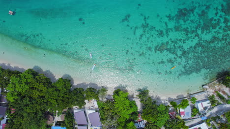 top down aerial view of turquoise blue beach shore with resort buildings and lush green tree tops