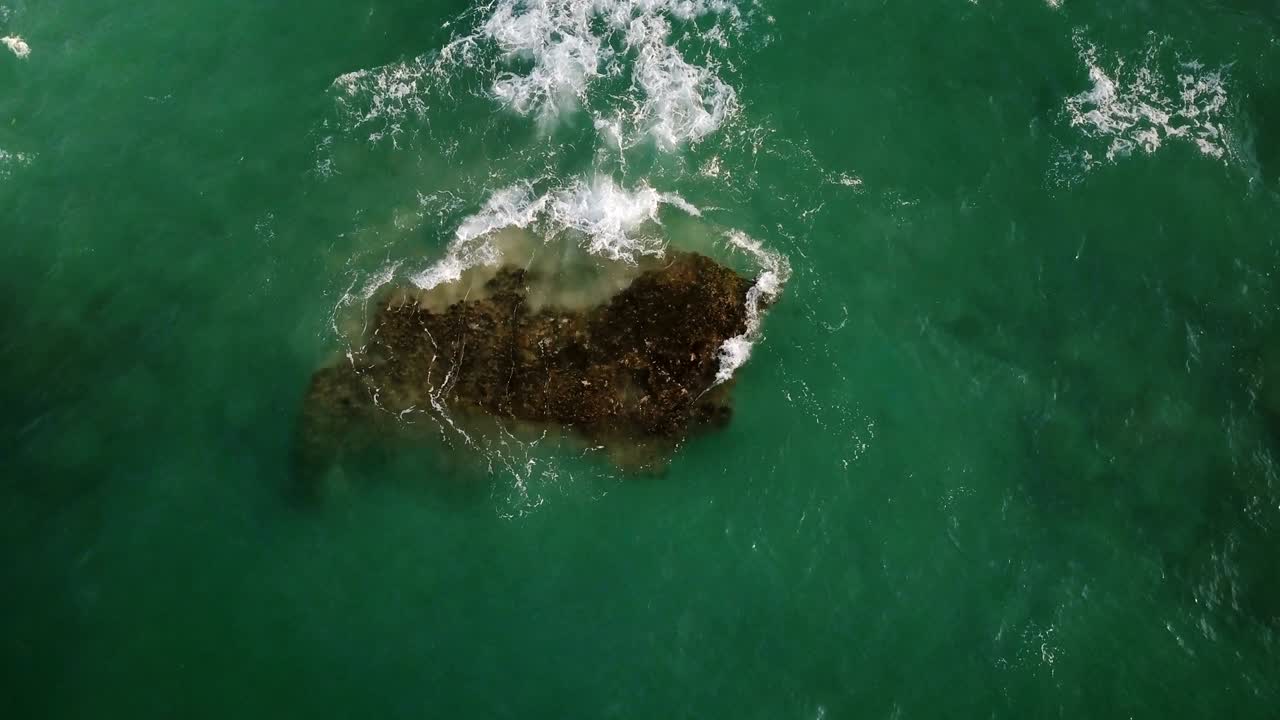 drone lockdown tiro de ondas verdes transparentes lavando sobre la piedra grande en el hermoso océano cerca de la costa, chocando con la espuma