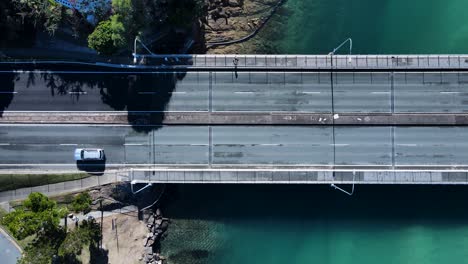 cars and pedestrians travel across a bridge spanning across a clear water scenic creek