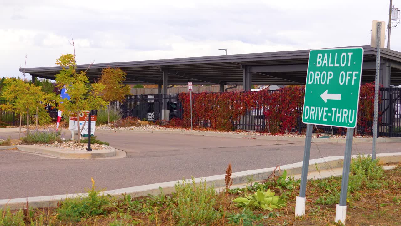 A clear election sign reads “Ballot Drop Off” with an arrow, standing near a road, symbolizing safe, secure, and accessible civic duty, democracy, equality, and the freedom to participate