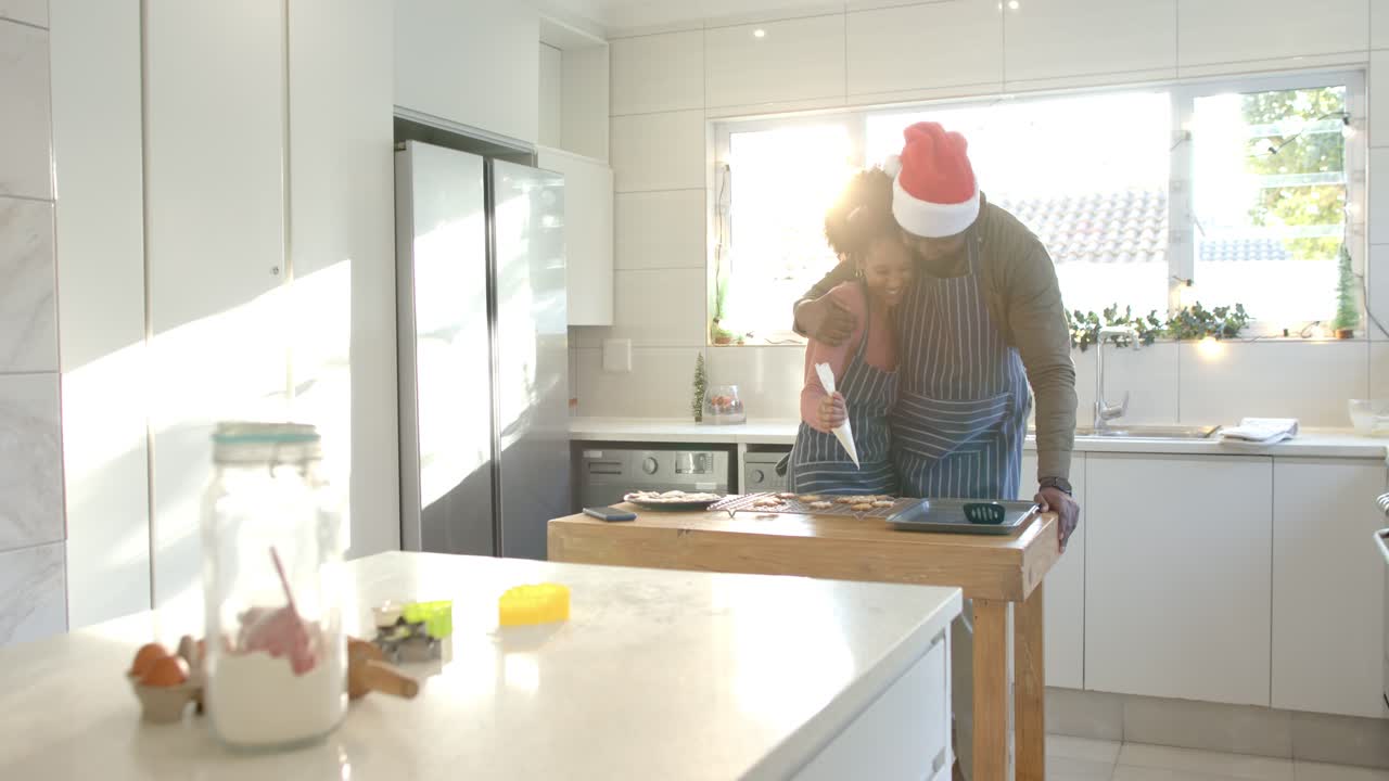 Diversa coppia che decora biscotti con una sac à poche per dolci festivi su un'isola in una cucina bianca