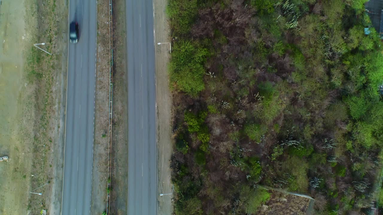 Top down drone follows highway road on tropical hillside, bird's eye view
