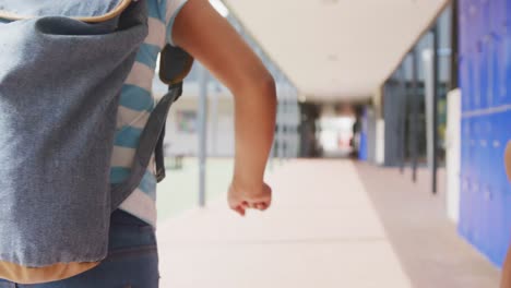Video-midsection-of-two-diverse,-children-with-schoolbags-running-in-school-corridor,-copy-space