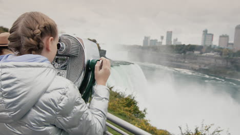 the girl looks through stationary binoculars at the beautiful landscape of niagara falls. famous landmark on the border of the united states and canada