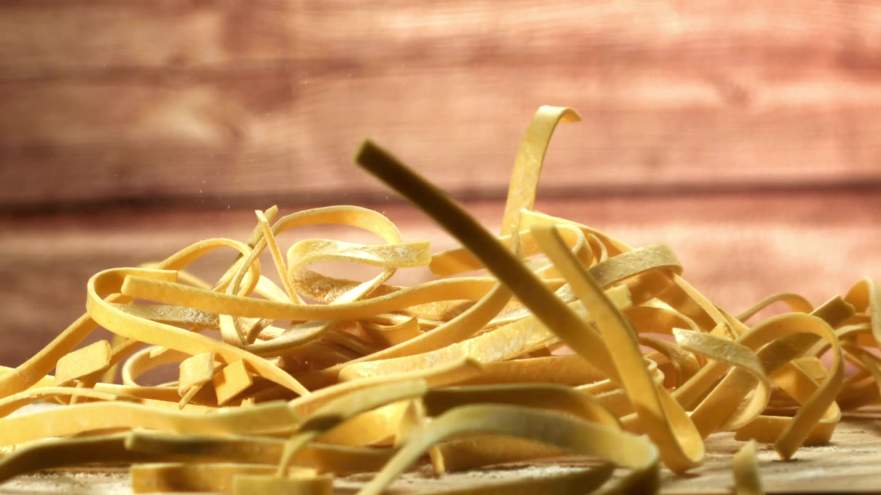 Tagliatelle fresche che cadono su una superficie di legno infarinata al rallentatore
