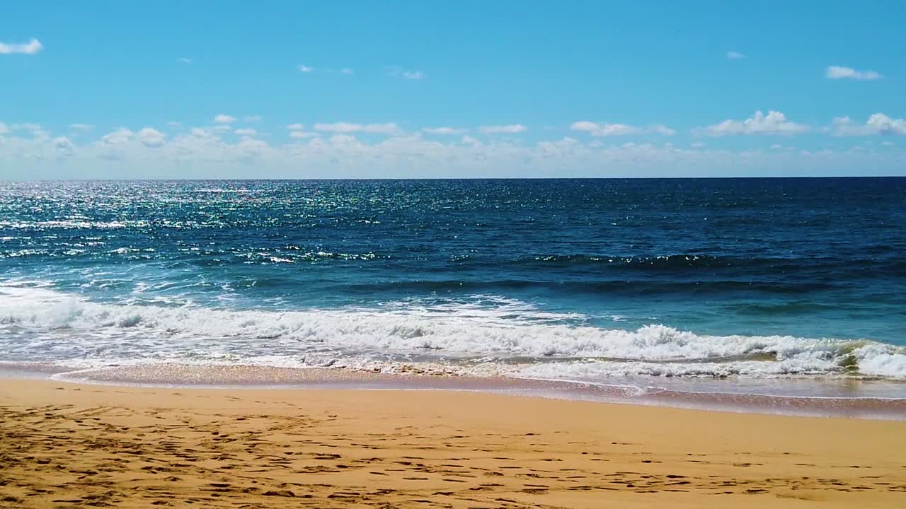 HD Hawaii Kauai slow motion beautiful backlit shot of ocean waves breaking on beach in lower third, ocean in middle third, clouds at horizon and blue sky in upper third version one