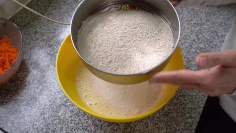 baker's hands sifting wholemeal flour with sieve in the kitchen