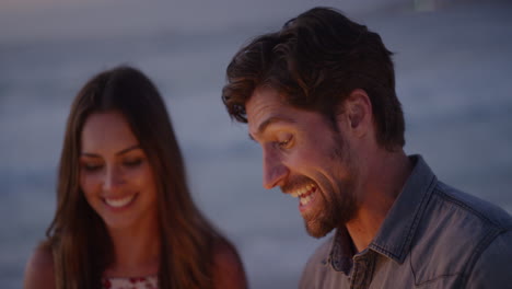 Feliz-Pareja-Joven-Celebrando-La-Víspera-De-Año-Nuevo-Hombre-Atractivo-Agitando-Bengalas-Disfrutando-De-La-Celebración-En-La-Playa-Tranquila-Al-Atardecer-Fuegos-Artificiales-Brillantes