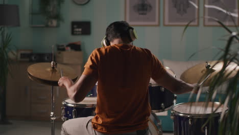 Rear View of Male Musician Playing Drums in Studio Talented Rock Drummer Rehearsing alone in Night Rear View of Male Musician Playing Drums in Studio Talented Rock Drummer Rehearsing alone in Night with Man Enjoying Music and Rhythm Express your Emotions Feelings and Talent