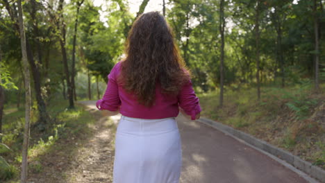 Pregnant-woman-smiles-at-camera,-flips-hair-over-to-fix,-turns-to-walk-park-path