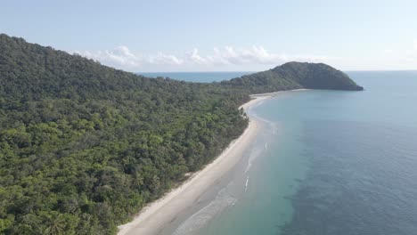 stretch of sandy foreshore with lush forest mountains at myall beach in daintree national park, queensland australia