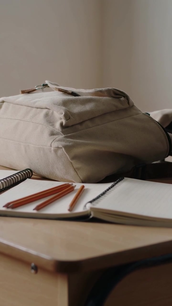 Vertical video: Hands entering right person in green tee placing beige backpack on desk preparing