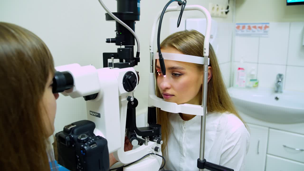 Pretty young woman do eye test sitting in front of doctor. Female optometrist is examining patient's eyes in medical office. Ophthalmology treatment.