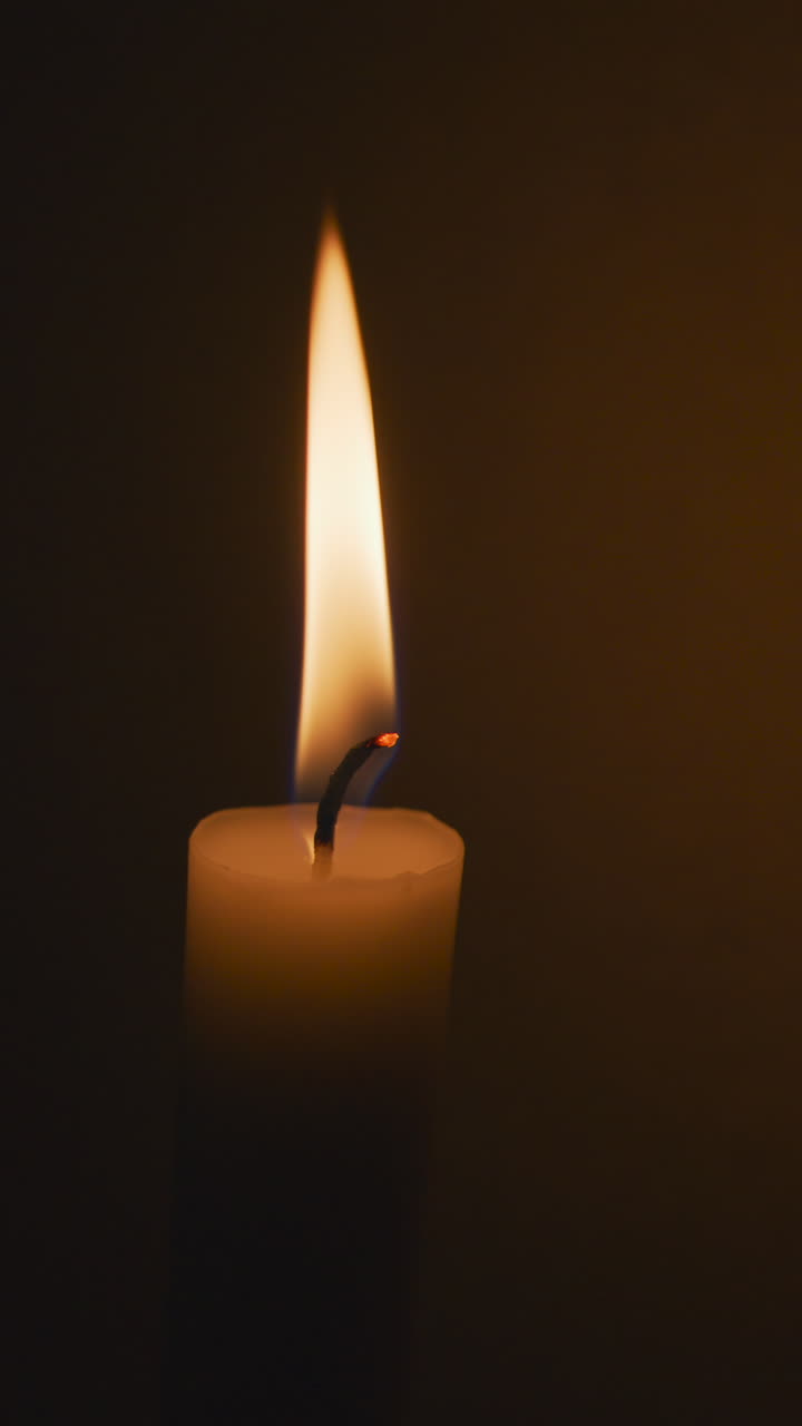 Primo piano di una candela a bastoncino accesa su uno sfondo nero. Verticale