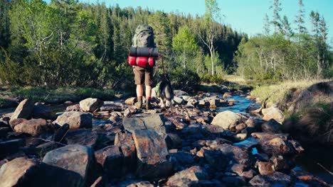 Wanderer-Mit-Seinem-Hund-überquert-Einen-Steinigen-Fluss