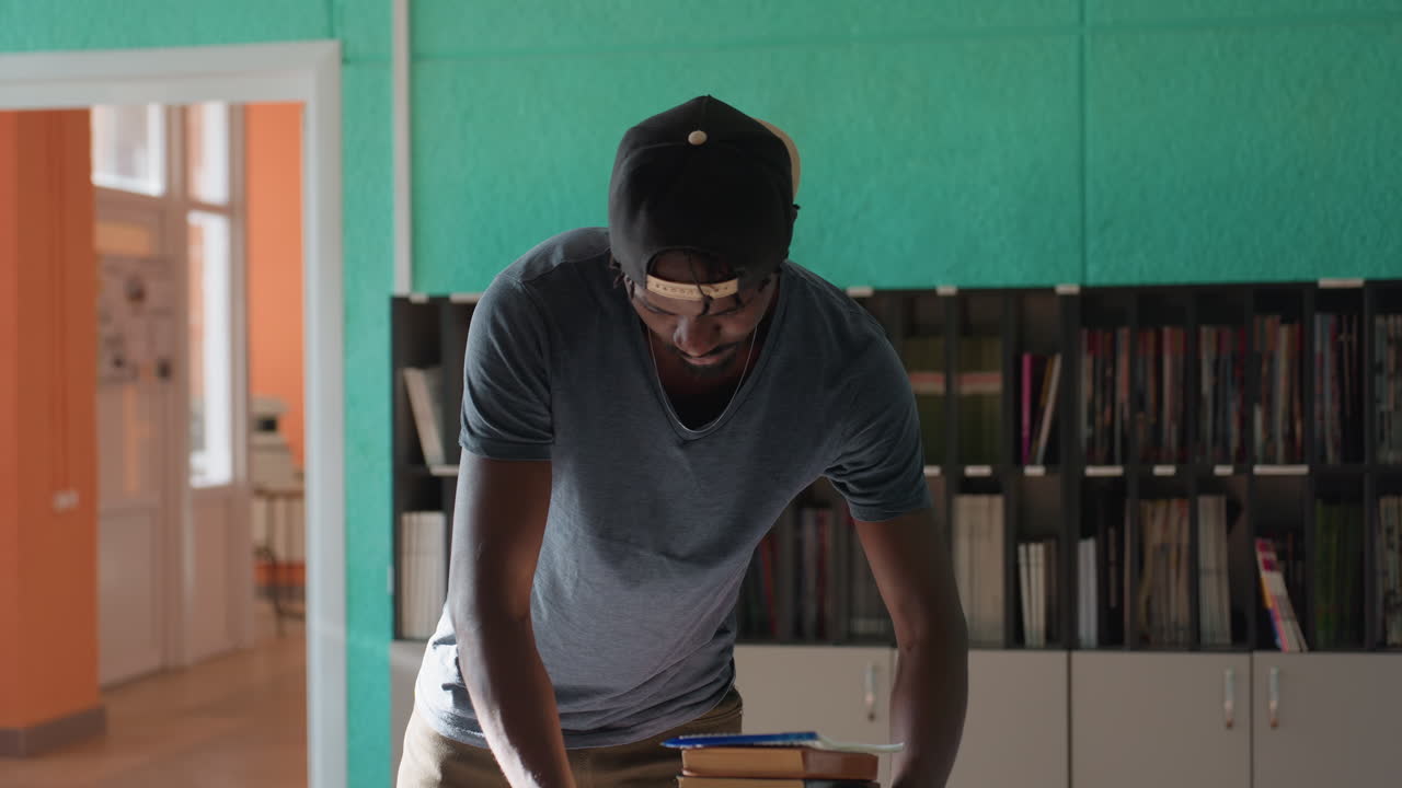 Student enters bright building holding stack of books, crossing large room past teal wall cabinets and clock then dropping books on desk bathed in sunlight, tidy shelves and minimalist decor around