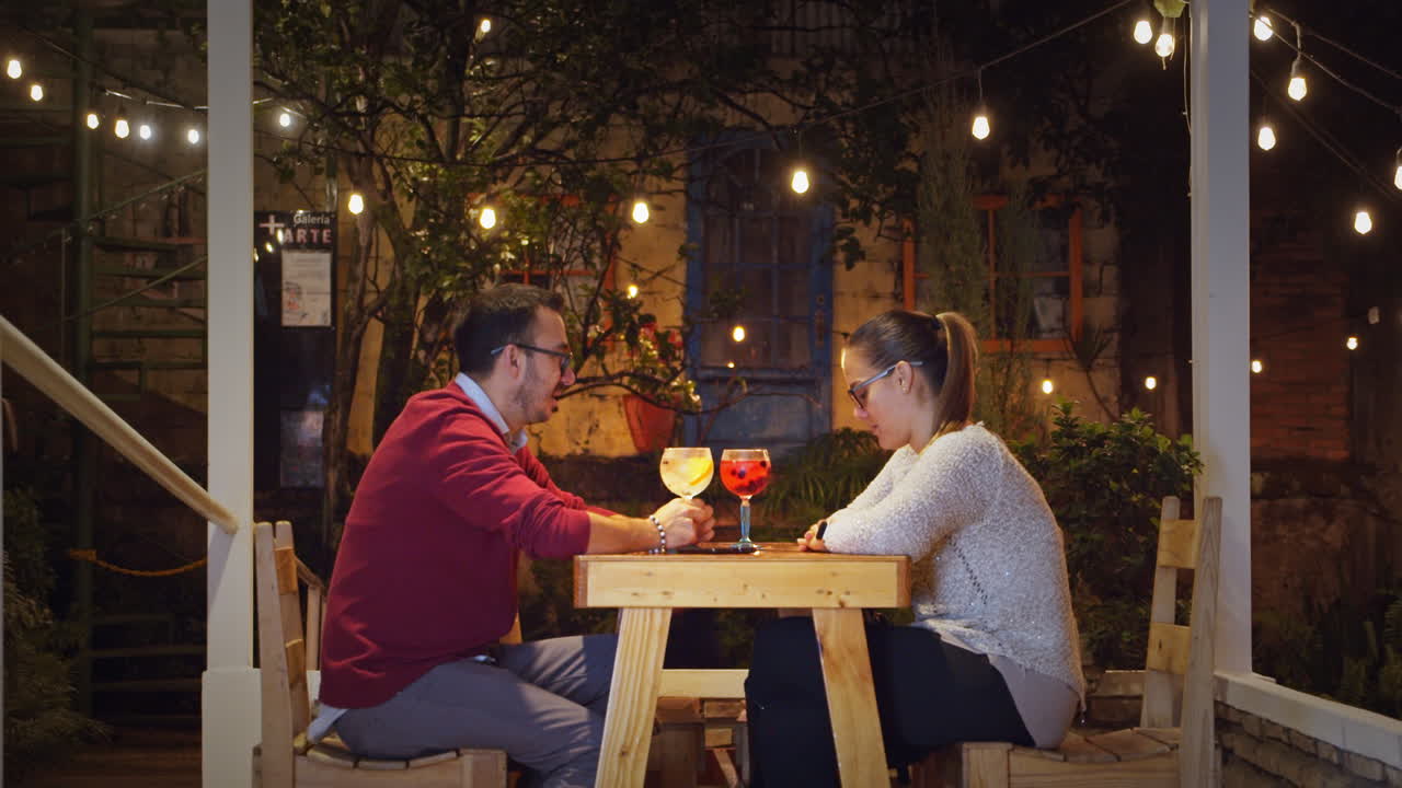 Couple Enjoying Drinks Outdoors Under String Lights at Night
