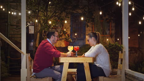 couple enjoying drinks outdoors under string lights at night