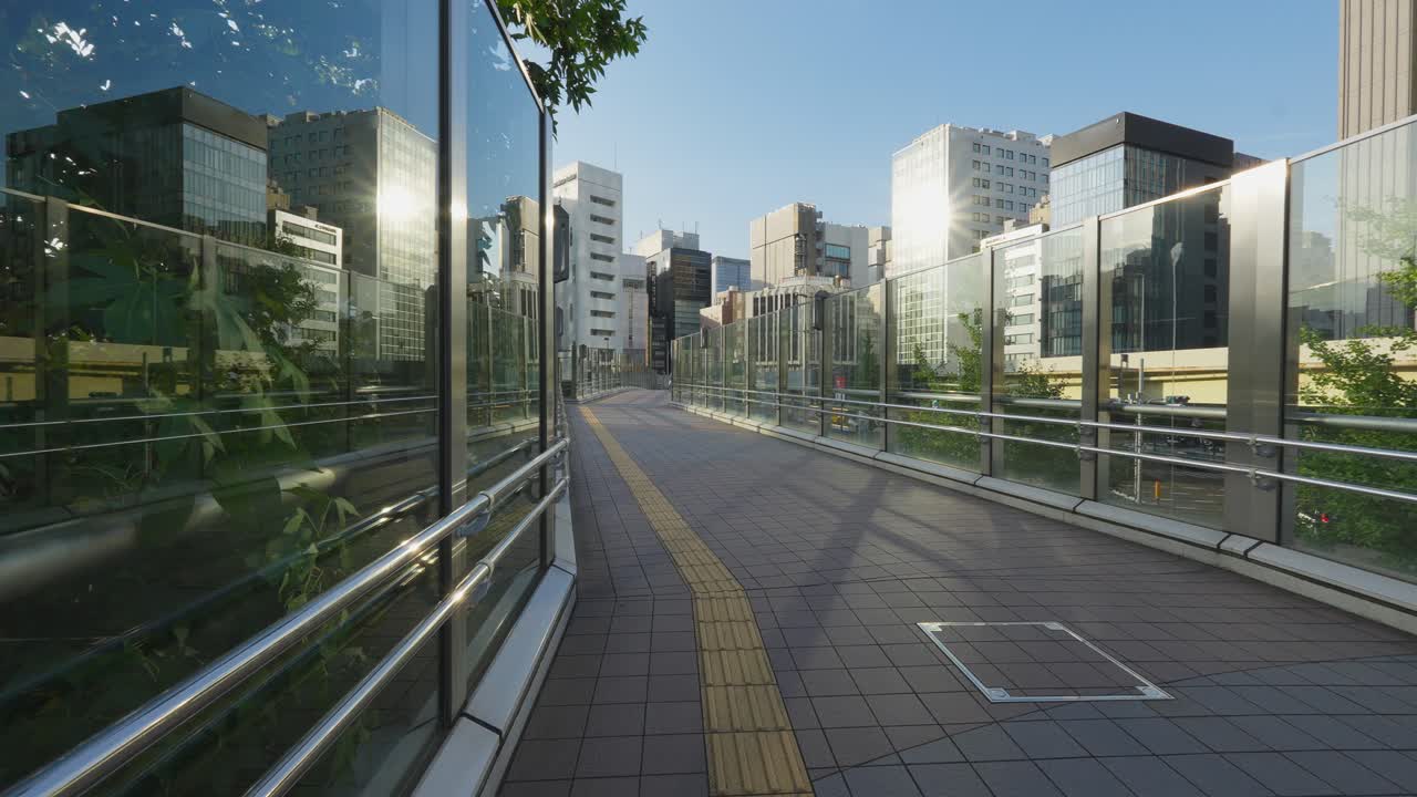 A bright and empty elevated pedestrian walkway with glass walls, surrounded by modern office buildings