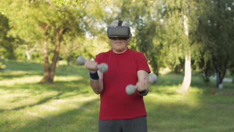 Senior-old-grandfather-man-in-VR-headset-helmet-making-fitness-exercises-with-dumbbells-outdoors