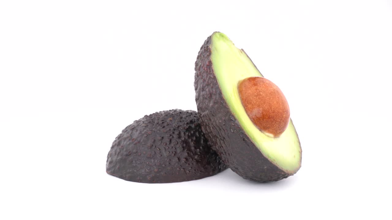 Due metà di avocado Haas affettato ruotano lentamente su un piatto girevole. Isolato su sfondo bianco. Macro ravvicinata