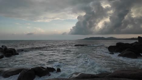 panning shot of vast ocean with waves crashing onto rocks, cloudy summer day