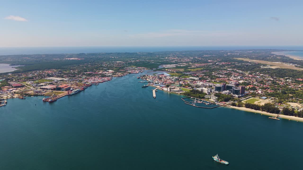 Pull-up aerial shot of Labuan Island, Malaysia, showing Victoria City skyline, coastline, and ships anchored offshore in calm blue waters