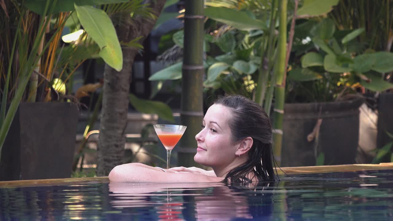 Plano Médio de uma Jovem Mulher Relaxando à Beira da Piscina Enquanto Desfruta de um Coquetel em um Hotel Tropical