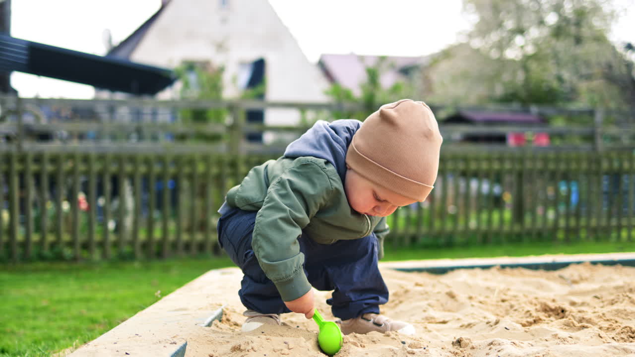 Smiling boy 2 years old playing in the sandbox on the playground. Toddler boy playing with sand on the street. Children's games outdoors