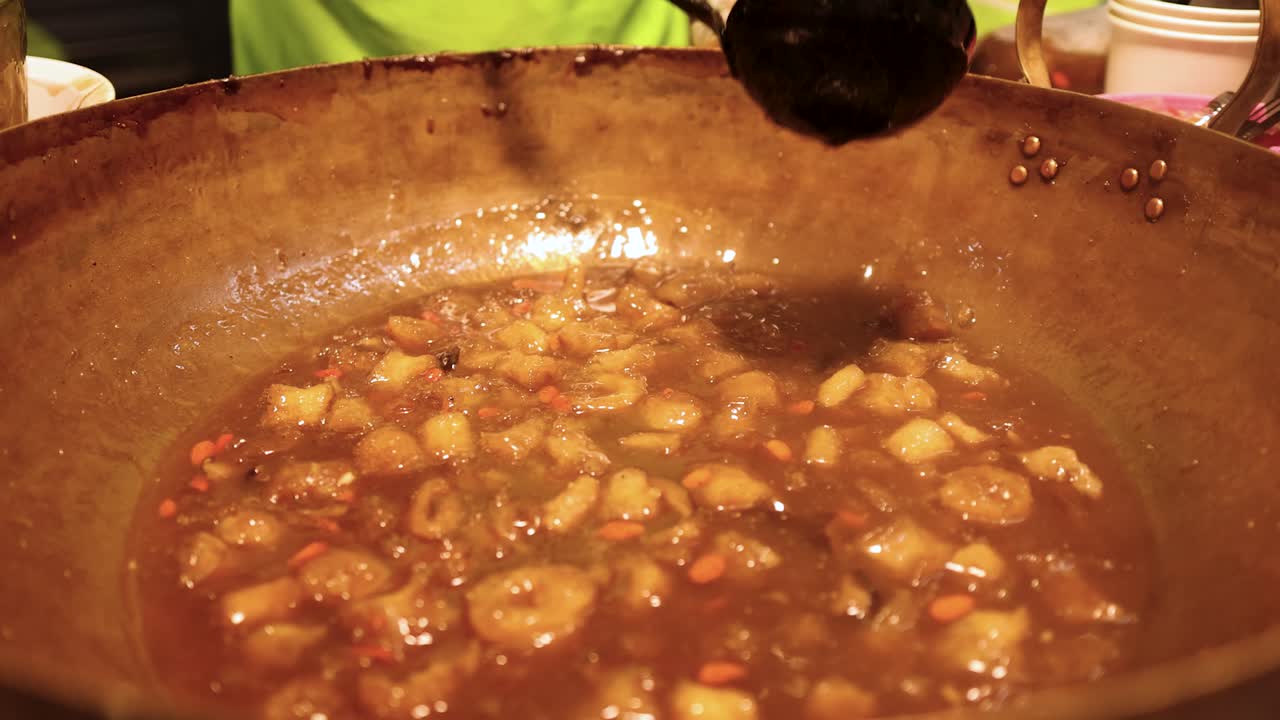 Vendor ladles steaming fish maw soup from large wok under warm street food lighting