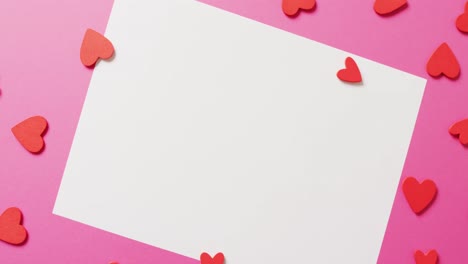 Video-of-red-paper-heart-shapes-and-black-white-sheet-of-paper-with-copy-space,-on-pink-background