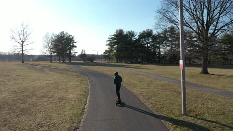 an aerial tracking of a man on an electric skateboard in an empty park on a sunny day