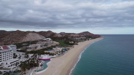 Vista-Aérea-Sobre-El-Hermoso-Paisaje-Costero-De-Marqués-Los-Cabos-Con-Vistas-Al-Lujoso-Hotel-Los-Cabos-Con-Mar-Azul-Y-Montañas-Al-Fondo,-Disparo-De-Drone-Giratorio