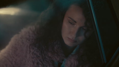 young thoughtful woman sitting in car, leaning against window, looking down